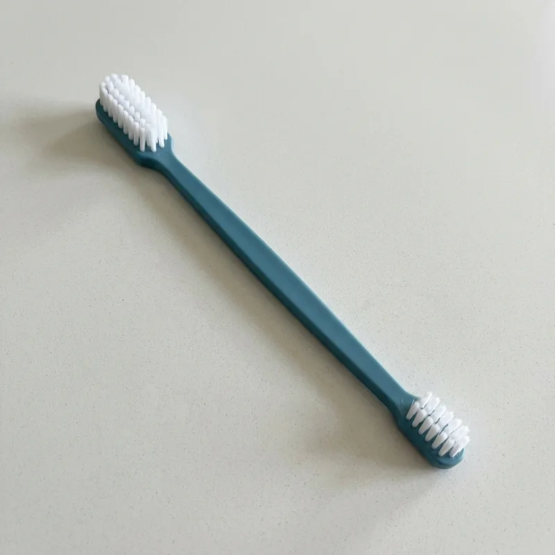 Double-ended pet toothbrush with a large and a small bristle head on a plain counter